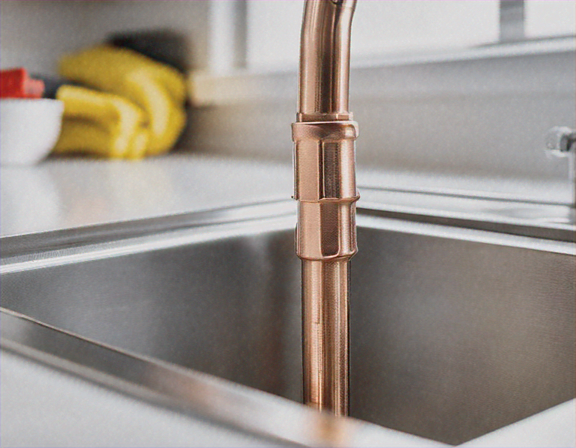 Close-up of plumber soldering copper pipe joints under a kitchen sink, natural light